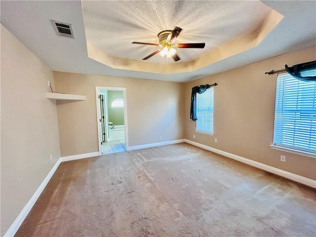 unfurnished room with a raised ceiling, ceiling fan, carpet flooring, and a textured ceiling