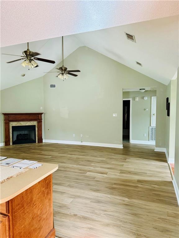 unfurnished living room featuring ceiling fan, a premium fireplace, high vaulted ceiling, and light hardwood / wood-style flooring