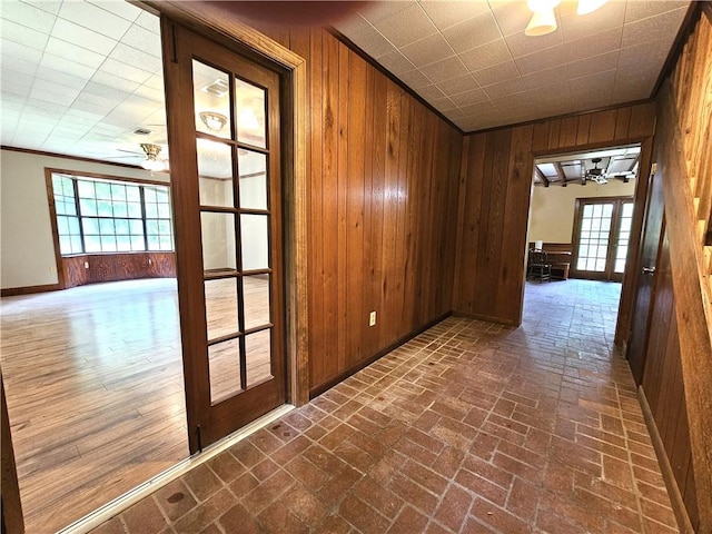 hall with an inviting chandelier, wood walls, crown molding, and french doors