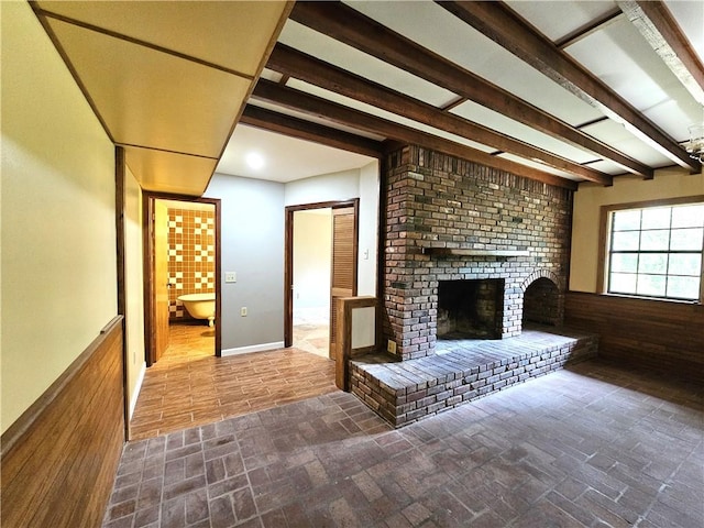 unfurnished living room featuring a brick fireplace, brick wall, and beam ceiling