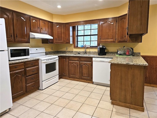 kitchen with dark brown cabinetry, light tile floors, light stone countertops, white appliances, and sink