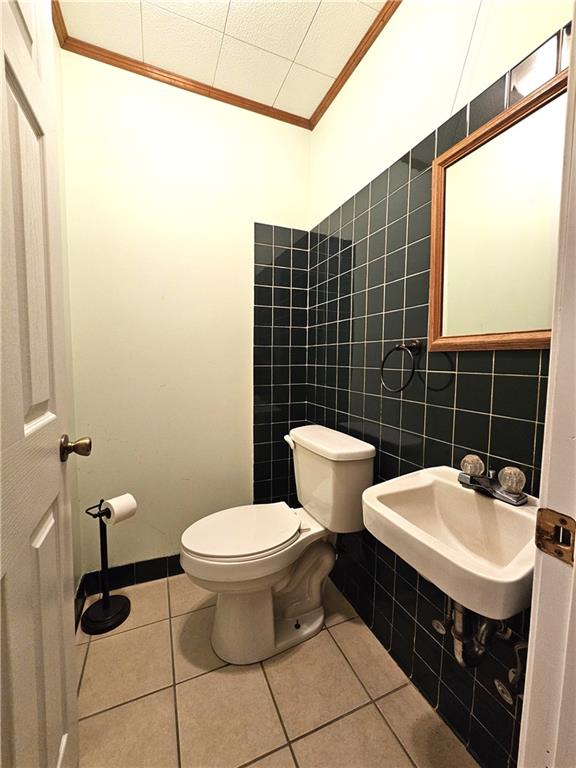 bathroom featuring ornamental molding, tile flooring, toilet, and tile walls