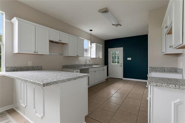 kitchen with light stone counters, white cabinetry, light tile floors, and sink