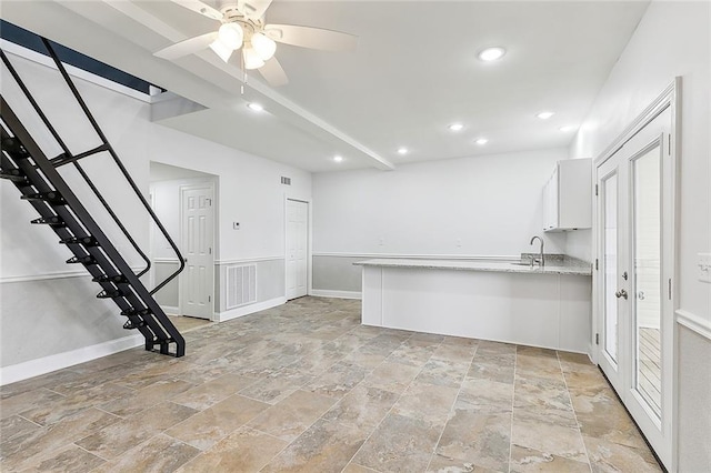 interior space with kitchen peninsula, ceiling fan, light tile floors, light stone counters, and white cabinets