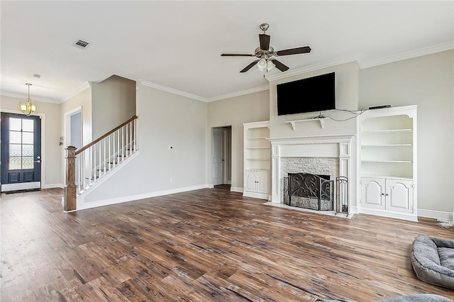 unfurnished living room with built in features, hardwood / wood-style floors, a fireplace, ceiling fan with notable chandelier, and ornamental molding