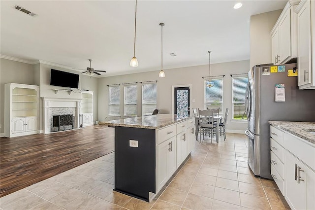 kitchen with white cabinets, light tile patterned floors, a kitchen island, and light stone counters