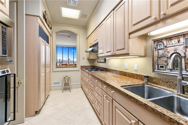 kitchen featuring dark stone counters, crown molding, light brown cabinetry, and sink