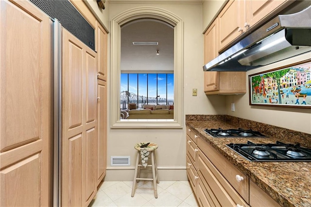 kitchen featuring dark stone counters, black gas cooktop, light brown cabinetry, and light tile patterned floors