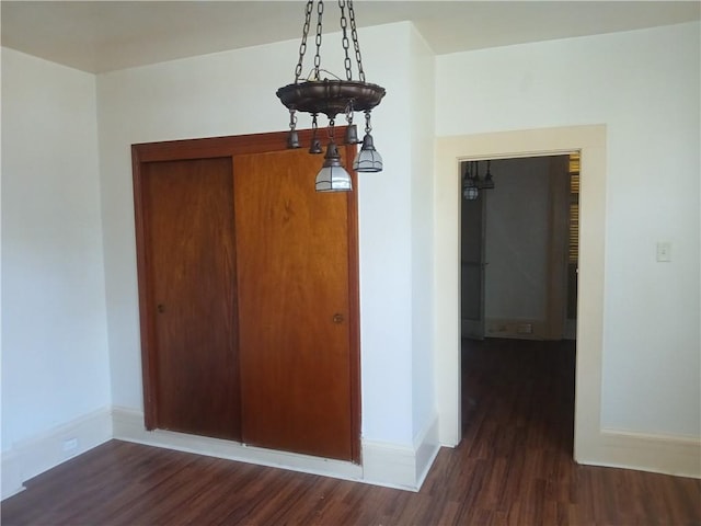 spare room with a chandelier and dark wood-type flooring