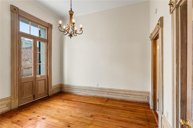 unfurnished dining area with hardwood / wood-style flooring, crown molding, and an inviting chandelier