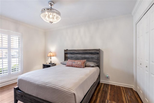 bedroom with dark hardwood / wood-style flooring, ornamental molding, a chandelier, and a closet