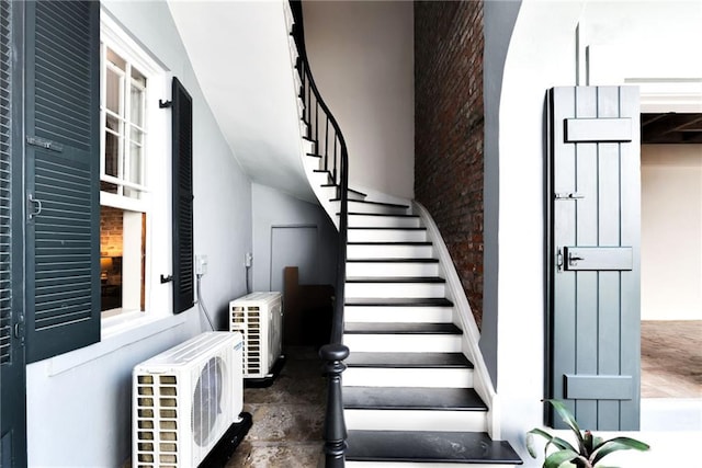 stairway featuring ac unit, brick wall, and a high ceiling