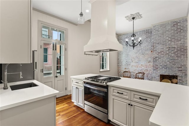 kitchen with white cabinetry, hanging light fixtures, stainless steel gas range oven, custom exhaust hood, and hardwood / wood-style flooring