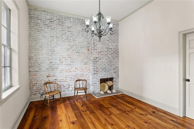 interior space with a brick fireplace, an inviting chandelier, brick wall, crown molding, and wood-type flooring