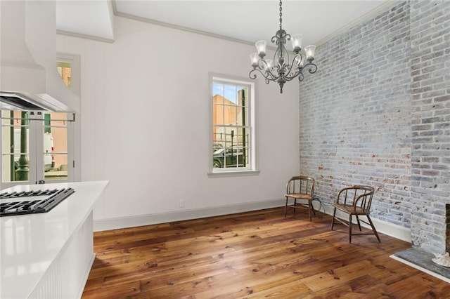 unfurnished dining area with hardwood / wood-style flooring, crown molding, brick wall, and an inviting chandelier