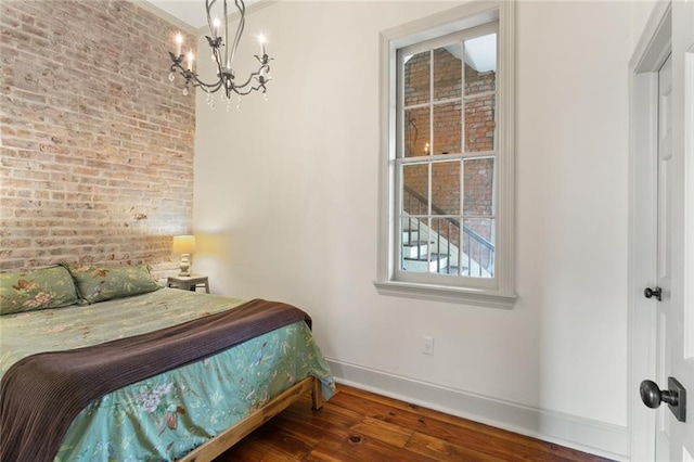 bedroom featuring dark hardwood / wood-style flooring, an inviting chandelier, and brick wall