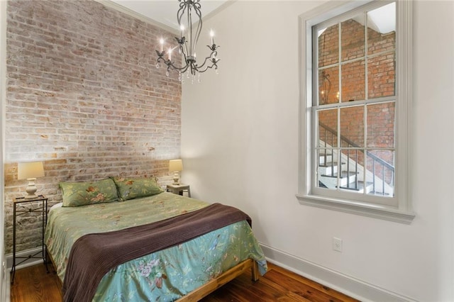 bedroom with hardwood / wood-style flooring, ornamental molding, brick wall, and an inviting chandelier