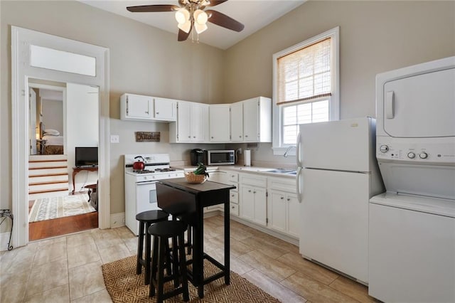 kitchen featuring white appliances, white cabinets, ceiling fan, and stacked washer / drying machine