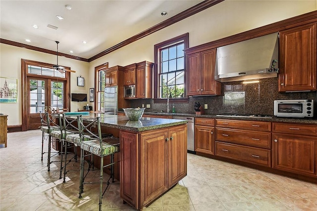 kitchen with french doors, a kitchen island, a kitchen bar, ceiling fan, and wall chimney range hood