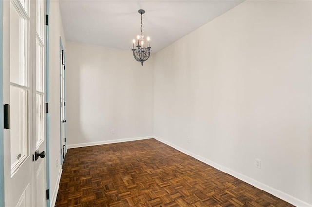 spare room with dark parquet floors and an inviting chandelier