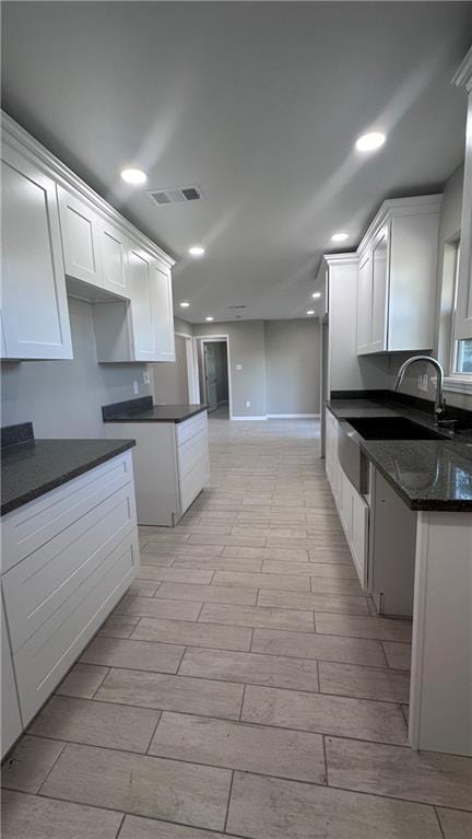 kitchen featuring dark stone countertops, white cabinets, and sink