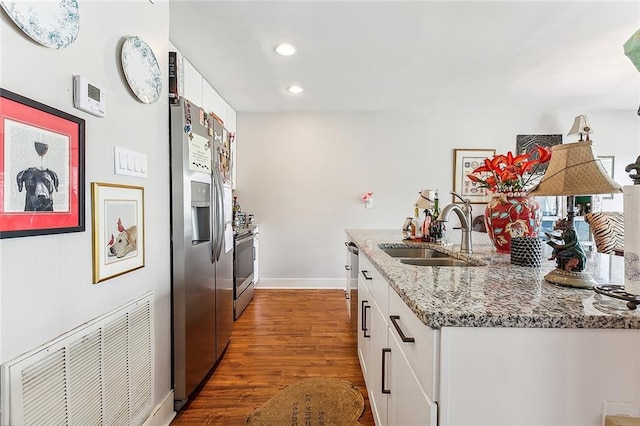 kitchen featuring light stone counters, appliances with stainless steel finishes, sink, white cabinetry, and dark wood-type flooring