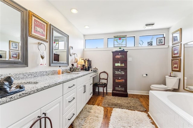 bathroom featuring a bath to relax in, hardwood / wood-style flooring, toilet, and double sink vanity