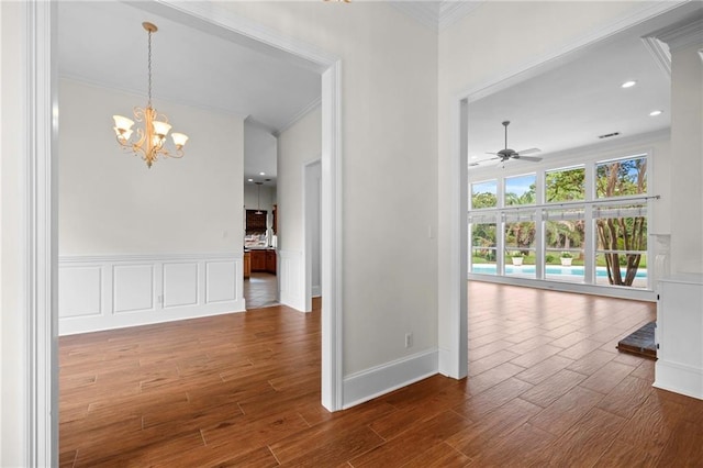 interior space with a wainscoted wall, wood finished floors, crown molding, a decorative wall, and a chandelier