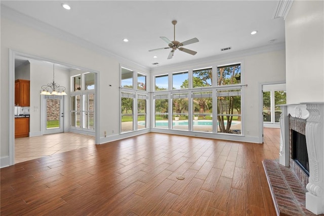 unfurnished living room with wood finished floors, visible vents, a fireplace, ornamental molding, and ceiling fan with notable chandelier