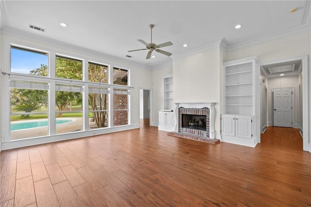 unfurnished living room featuring visible vents, wood finished floors, crown molding, a brick fireplace, and attic access