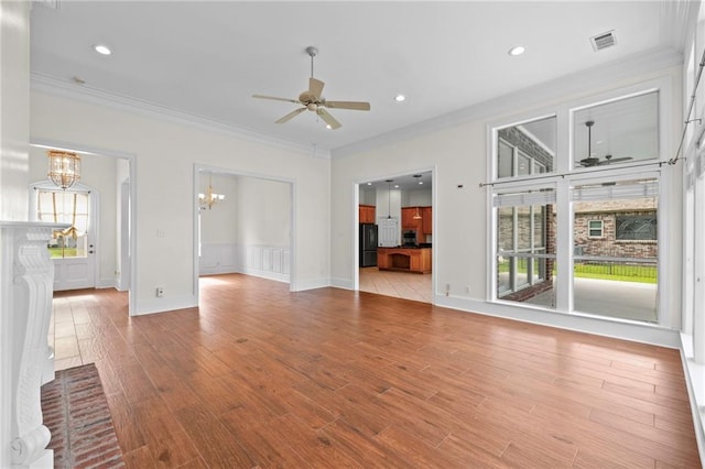 unfurnished living room with ceiling fan with notable chandelier, visible vents, light wood finished floors, and ornamental molding