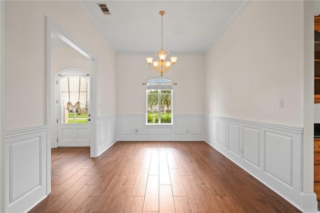 unfurnished dining area with visible vents, an inviting chandelier, wood finished floors, and crown molding