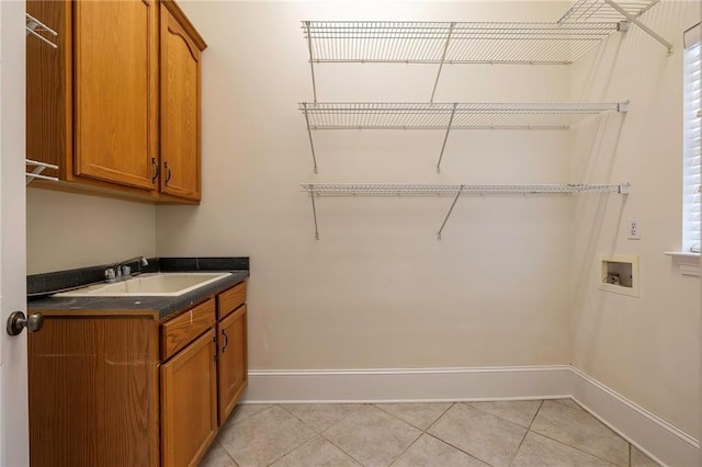 laundry room featuring light tile patterned floors, baseboards, cabinet space, a sink, and washer hookup