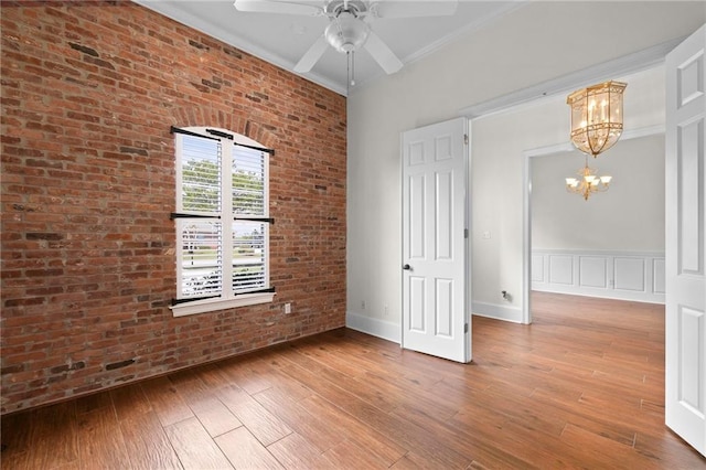 spare room featuring ceiling fan with notable chandelier, wood finished floors, brick wall, crown molding, and a decorative wall