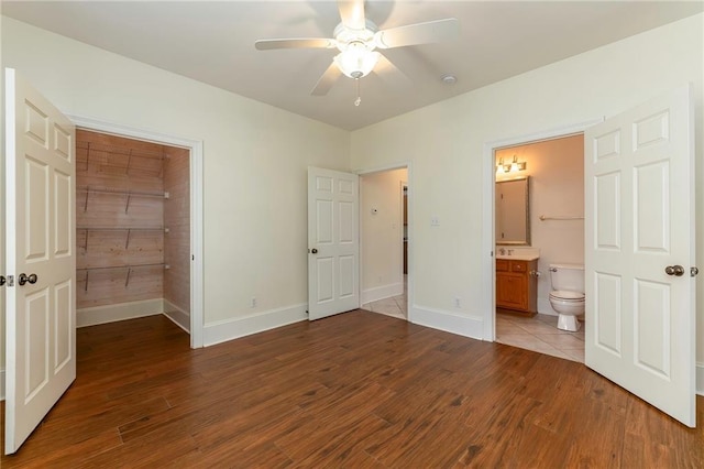 unfurnished bedroom featuring a spacious closet, wood finished floors, baseboards, and ensuite bathroom