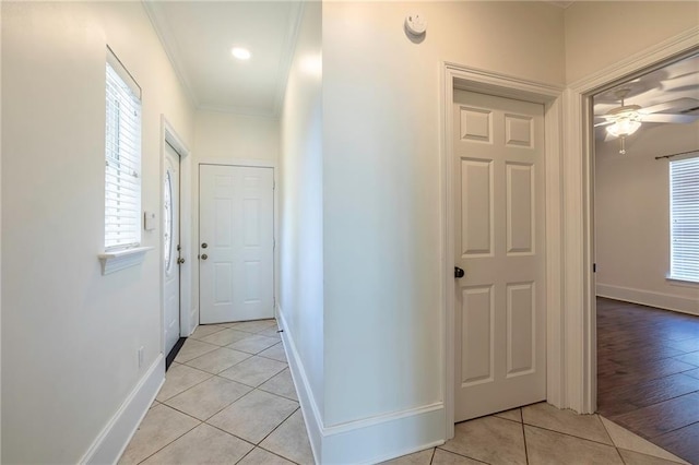 hall with crown molding, light tile patterned flooring, and a healthy amount of sunlight