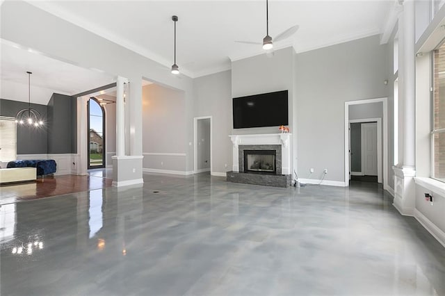 unfurnished living room with a high ceiling, ceiling fan with notable chandelier, decorative columns, and a premium fireplace