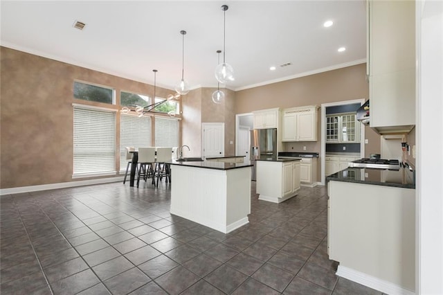 kitchen featuring stainless steel appliances, white cabinets, decorative light fixtures, dark tile flooring, and a center island with sink