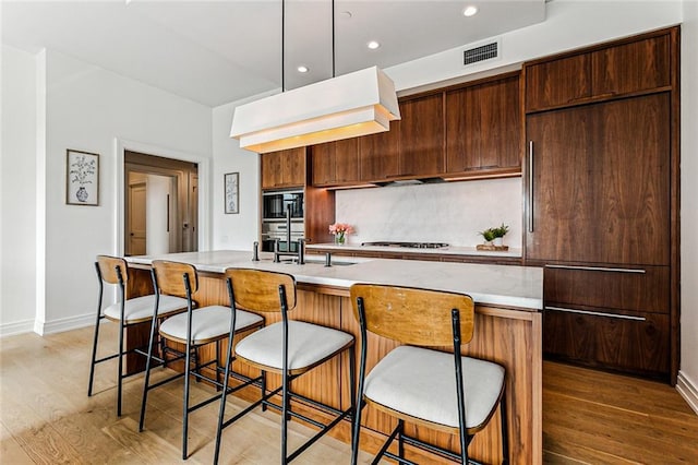 kitchen with a kitchen island with sink, hardwood / wood-style flooring, decorative backsplash, and a kitchen bar