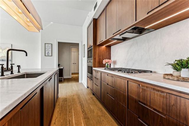 kitchen with tasteful backsplash, stainless steel appliances, sink, and light wood-type flooring