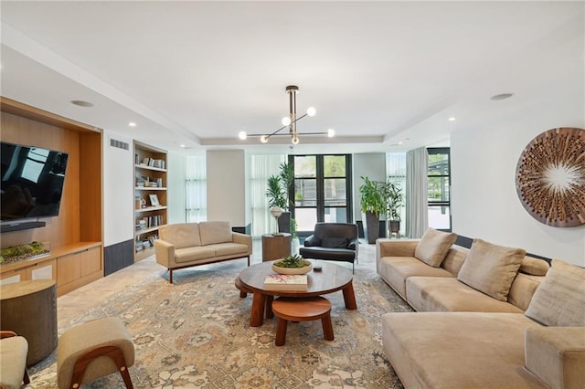 living room featuring built in features, a raised ceiling, and a chandelier