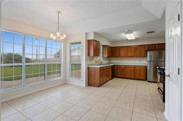 kitchen featuring light tile floors, range, an inviting chandelier, stainless steel refrigerator, and pendant lighting