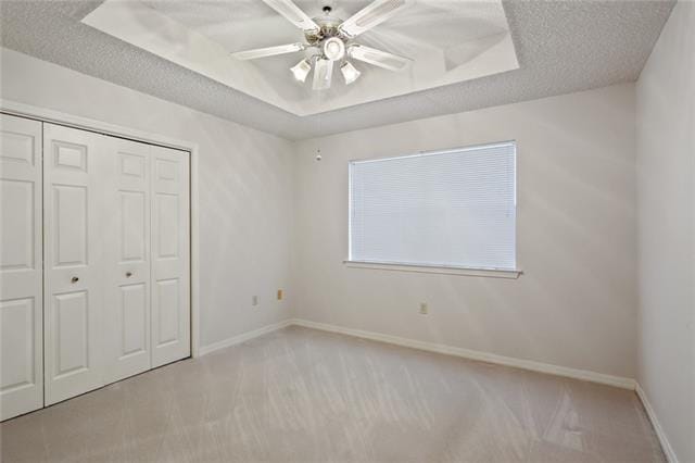 unfurnished bedroom featuring a textured ceiling, ceiling fan, light colored carpet, and a raised ceiling