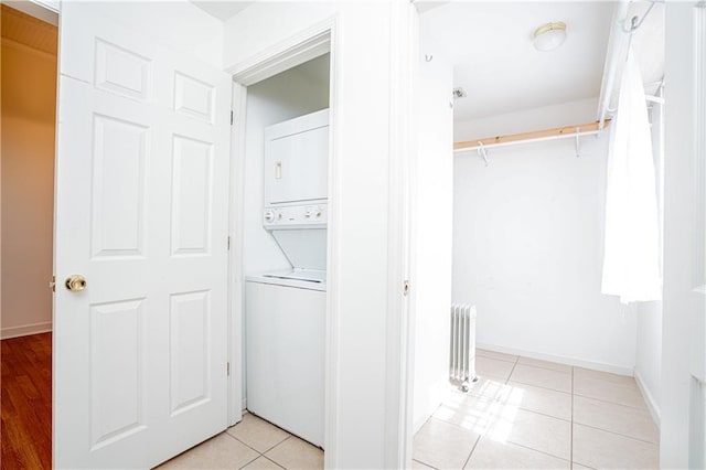 washroom featuring light tile patterned floors, stacked washer and dryer, and radiator heating unit