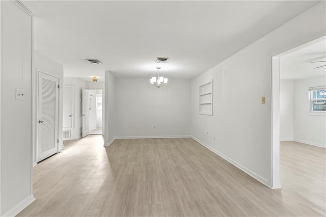 empty room with ceiling fan with notable chandelier and light hardwood / wood-style floors