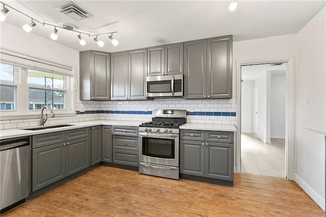 kitchen with appliances with stainless steel finishes, gray cabinets, light hardwood / wood-style flooring, and sink