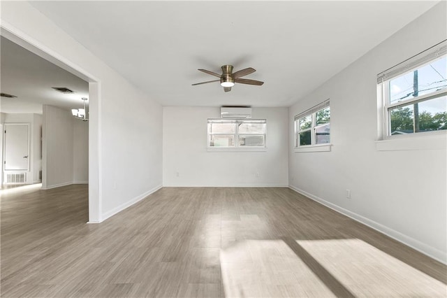 empty room featuring ceiling fan with notable chandelier, wood-type flooring, and a wall mounted AC