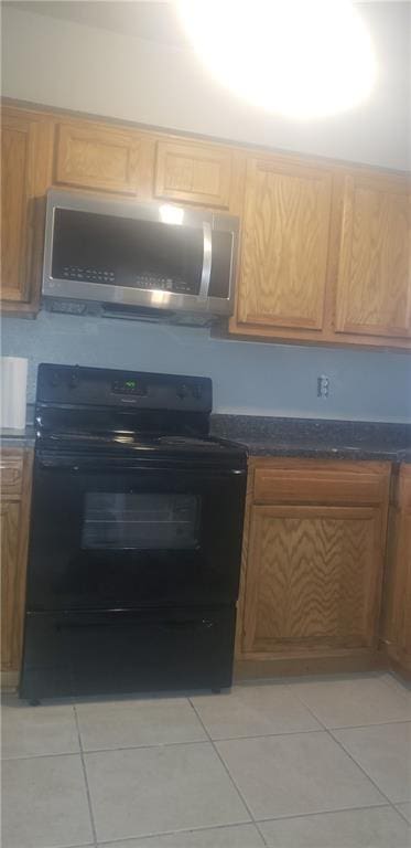 kitchen featuring black range with electric stovetop, light tile flooring, and dark stone counters