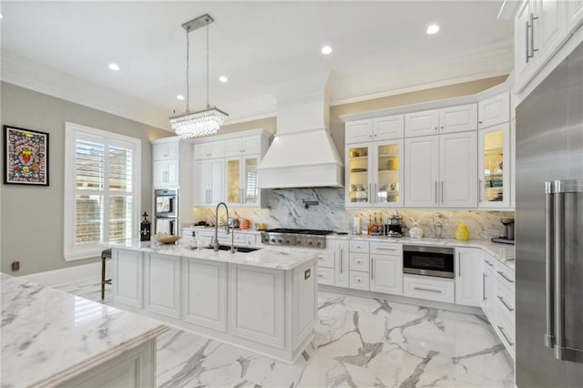 kitchen featuring sink, built in appliances, an island with sink, pendant lighting, and custom range hood