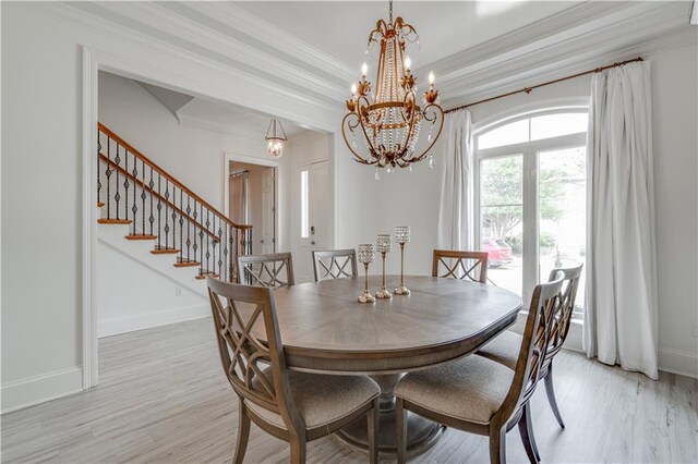 dining room featuring ornamental molding, a notable chandelier, light hardwood / wood-style flooring, and a tray ceiling